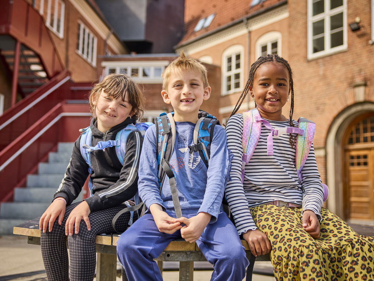 Tre skolebørn som sidder på et bord ude i skolegården