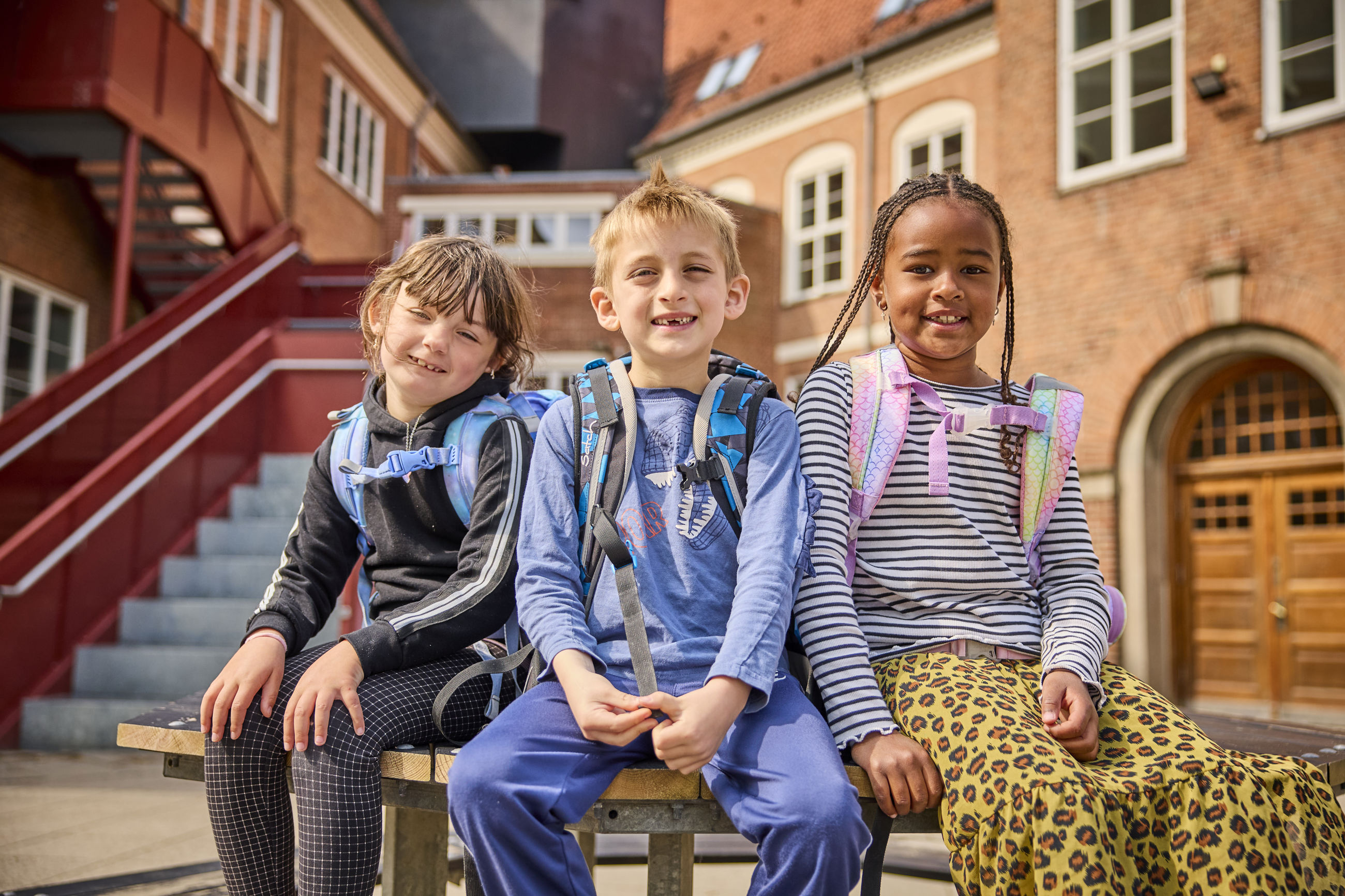 Tre skolebørn som sidder på et bord ude i skolegården